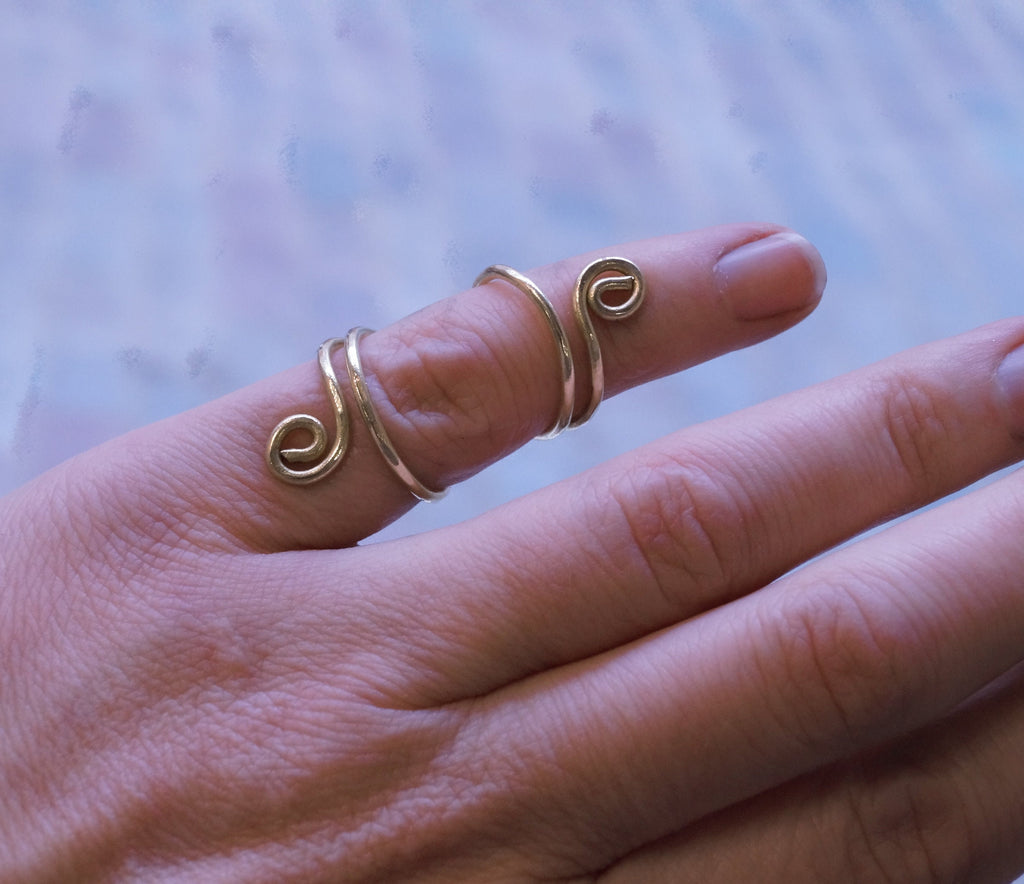 Hand wearing three gold spiral rings on a blurred background