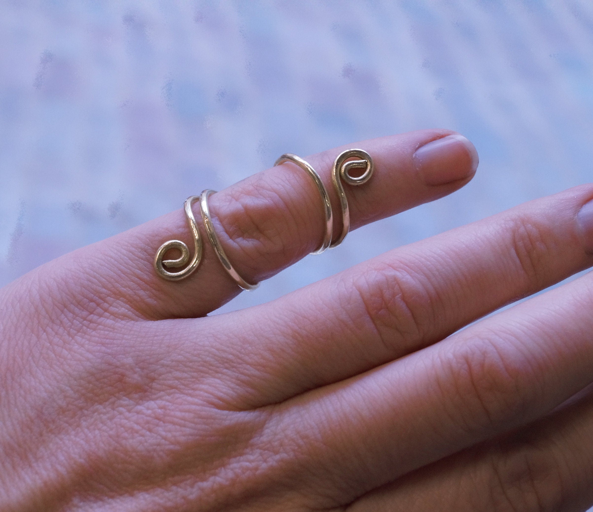 Hand wearing three gold spiral rings on a blurred background